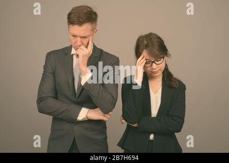 Studio shot of young handsome businessman et jeune belle Asian businesswoman wearing eyeglasses contre l'arrière-plan gris Banque D'Images