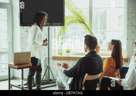 Sourire. Enceinte afro-américaine féminine donnant une présentation dans la salle à l'atelier. Public ou salle. Vue latérale des participants. Conférence, formation. Éducation, diversité, concept inclusif. Banque D'Images