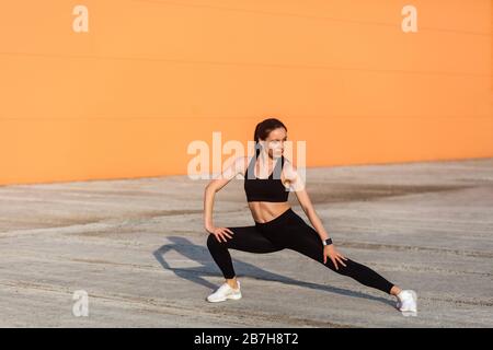 Jeune femme mince et jolie avec des vêtements de sport serrés, un pantalon et un haut noirs, pratiquant l'extérieur, faisant des entraînements étirements pour une plus grande flexibilité, un exe de bas-corps Banque D'Images