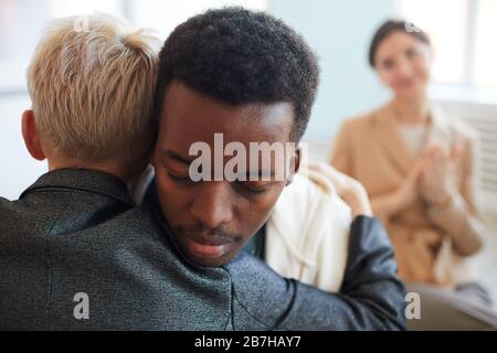 Vue arrière de la psychologue féminine embrassant l'adolescent afro-américain pendant la séance de thérapie dans le groupe de soutien, espace de copie Banque D'Images