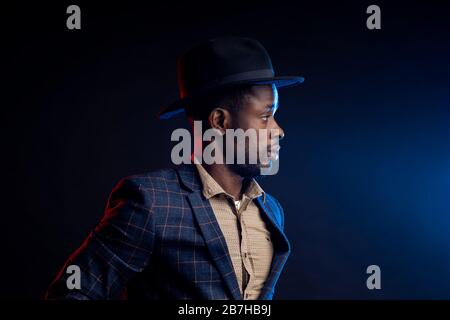 Portrait studio taille haute de jeune homme d'affaires africain peu rasé, confiant et sérieux, portant une chemise, costume à damier debout contre le noirceur Banque D'Images