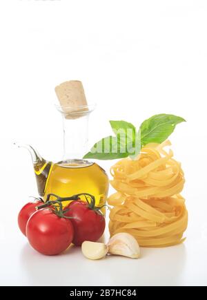 Concept de recette de pâtes. Nids de tagliatelle non cuits, basilic, tomates, huile d'olive et ail isolés sur fond blanc. Préparaa de nourriture italienne traditionnelle Banque D'Images