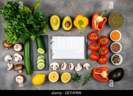 Différents légumes et ingrédients pour cuisiner de délicieux plats. Un livre pour écrire des recettes se trouve sur une table entourée de nourriture. Espace de copie pour le texte Banque D'Images