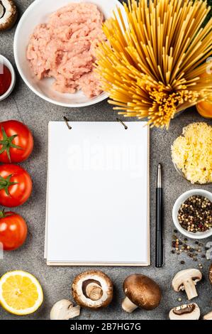 Différents légumes et ingrédients pour faire des pâtes. Un livre pour écrire des recettes se trouve sur une table entourée de nourriture. Espace de copie pour le texte Banque D'Images