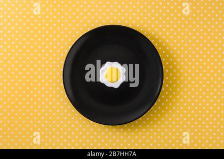Oeuf frit minimaliste sur plaque noire et fond jaune Banque D'Images