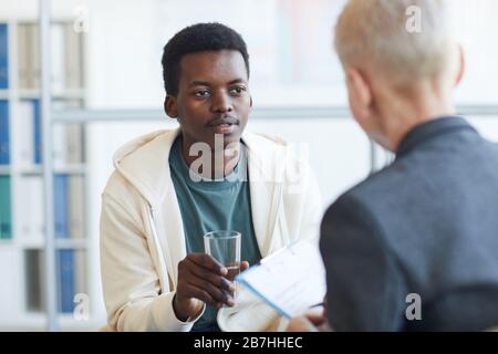 Portrait du jeune homme afro-américain tenant un verre d'eau pendant la séance de thérapie, espace de copie Banque D'Images