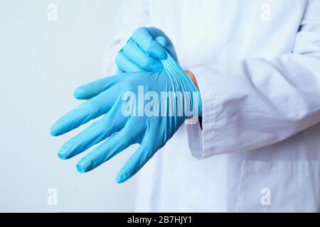 closeupo d'un homme de docteur caucasien, portant un manteau blanc, mettant sur une paire de gants chirurgicaux bleus Banque D'Images