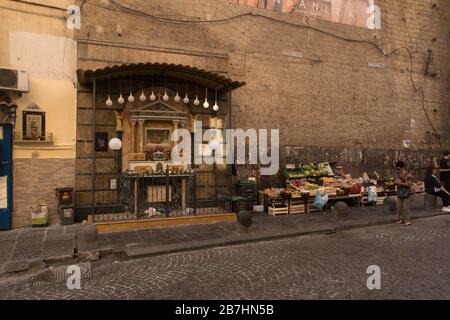 Sanctuaire de la Vierge Marie à côté d'un étalage de vente de fruits et légumes frais sur le pavé d'une rue du centre-ville de Naples, Italie Banque D'Images