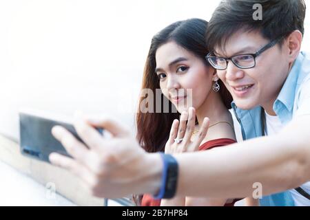 jeune homme asiatique utilisant un smartphone prenant des photos avec sa petite amie après avoir engagé la proposition et sourire heureuse femme et montrant son anneau de mariage. heureux Banque D'Images