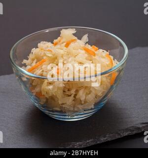 Chou fermenté maison avec carotte dans un bol en verre sur tableau en pierre noire. Salade végétalienne. Le plat est riche en vitamine U. Grande nourriture pour une bonne santé. Banque D'Images