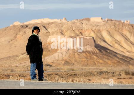 Berger de chèvre Froendly debout devant les ruines de l'ancienne forteresse Ayaz-Kala site archéologique, le désert de Kyzylkum, Karakalpakstan, Ouzbékistan Banque D'Images