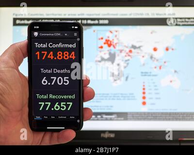 Italie, le 16 mars 2020 - les gens ont un smartphone avec des statistiques en direct actualisées sur le coronavirus COVID-19 et une carte des états infectés en arrière-plan Banque D'Images