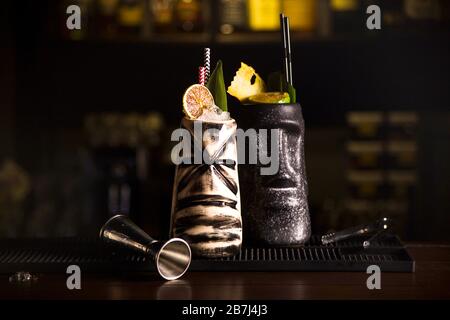 Tiki buvez des cocktails. Deux cocktails dans différents verres sur le fond d'un bar décoré de fruits secs et de feuilles tropicales. Banque D'Images