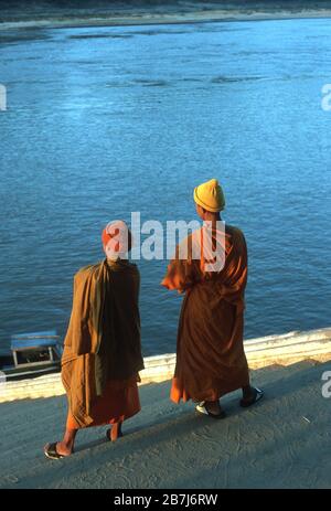 Deux moines bouddhistes en peignoirs orange se tiennent sur des marches menant au Mékong au coucher du soleil à Luang Prabang, au Laos. La ville de Luang Prabang est classée au patrimoine mondial de l'UNESCO. Banque D'Images