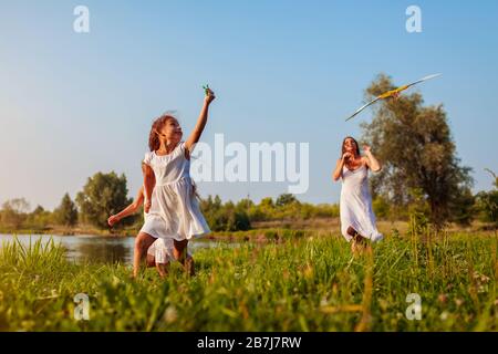 Fête des mères. Les filles heureuses qui courent avec le cerf-volant dans le parc d'été tandis que la mère les aide. Les enfants s'amusent à jouer à l'extérieur Banque D'Images