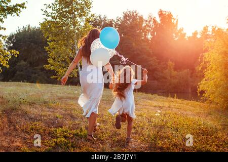 Fête des mères. Petite fille courir avec la mère et tenir des balons dans la main. Famille s'amuser dans le parc d'été Banque D'Images