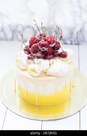 Gâteau blanc et jaune avec chocolat fondu et cerises fraîches sur le dessus. Fond blanc. Banque D'Images