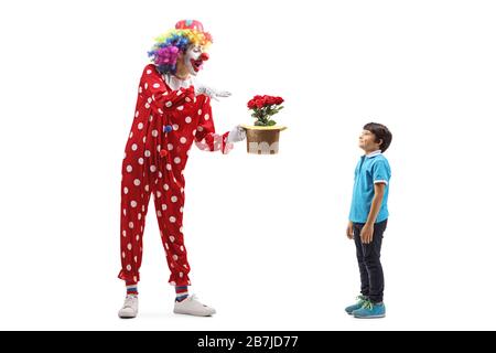 Photo pleine longueur d'un clown exécutant un tour avec des fleurs et un chapeau devant un garçon isolé sur fond blanc Banque D'Images