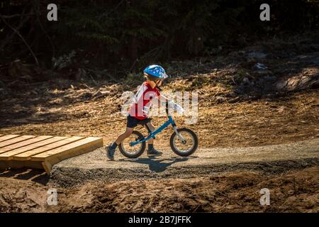 enfant de 2-3 ans sur un vélo de course, avec des lunettes de soleil et un casque, sur une piste de pompe de parc à vélo Banque D'Images