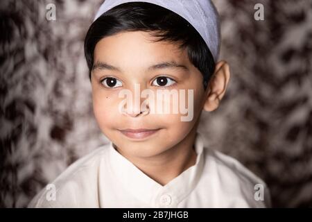 Portrait d'enfant musulman avec casquette musulmane et robe ethnique blanche donnant l'expression vers la lumière Banque D'Images