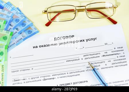 Document en russe « Contrat de fourniture de services immobiliers », lunettes, argent et stylo sur la table. Travaille sur la sélection et la vente de réel e Banque D'Images