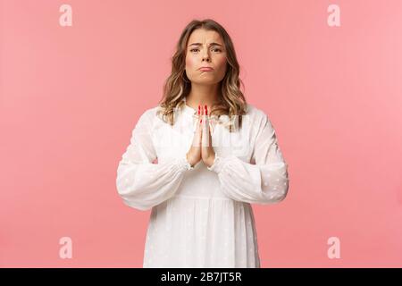 Portrait d'une petite amie pleine d'espoir, blonde fille mendiant pour la faveur en robe blanche sur fond rose, sobbing faire des yeux mignons, pleurer ou prier, Banque D'Images