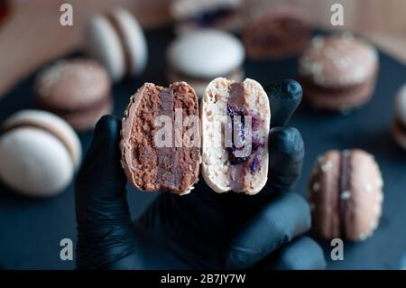 Les gants noirs contiennent deux moitiés de macaron avec ganache au chocolat Banque D'Images