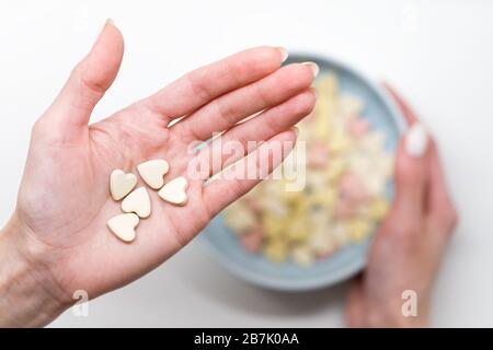 Près de la femme tient des vitamines en forme de coeur ou des pilules minérales sur la paume, main trouble tenant bol de vitamines colorées sur fond blanc, vue de dessus. F Banque D'Images