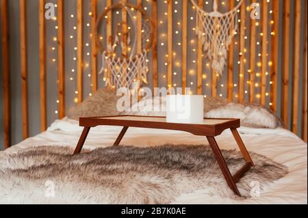 Table en bois vide plateau de petit-déjeuner dans le lit. Chambre Boho, décoration murale en bois avec guirlandes, lampes et trancheuses de rêve. Banque D'Images