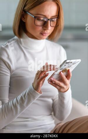 Une femme d'affaires sérieuse porte un pull blanc à col roulé et des lunettes dans un étui en marbre, naviguer sur Internet, acheter des produits en ligne, fond flou. Réseau social Banque D'Images