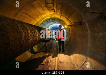 Le travailleur du tunnel examine le pipeline dans le tunnel souterrain Banque D'Images