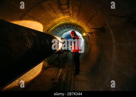 Le travailleur du tunnel examine le pipeline dans le tunnel souterrain. Banque D'Images