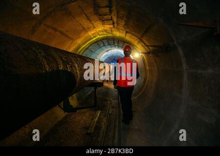 Le travailleur du tunnel examine le pipeline dans le tunnel souterrain Banque D'Images