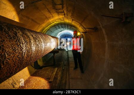 Le travailleur du tunnel examine le pipeline dans le tunnel souterrain Banque D'Images