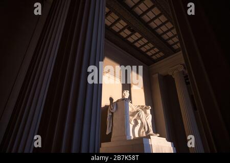 Lincoln Memorial Statue Sunrise Washington DC // WASHINGTON DC, USA - la grande statue à l'intérieur de la chambre principale du Lincoln Memorial captant la lumière dorée tôt le matin au lever du soleil pendant l'équinoxe d'automne (automne). Le Lincoln Memorial se trouve à l'extrémité ouest du bassin réfléchissant et fait face directement à l'est. La statue est profondément dans la chambre et est normalement bien hors de portée de la lumière directe du soleil. Banque D'Images