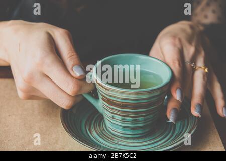 Les mains des femmes tiennent une tasse en céramique verte avec un motif original de style japonais. Image dans un style rétro vintage Banque D'Images