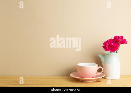 Tasse à café avec fleur de carnation vaporisée dans vase sur table en bois avec fond brun. Arrangement floral, espace de copie Banque D'Images