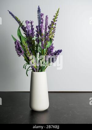 Vase en céramique blanc simple rempli de fleurs violettes sur fond d'ardoise noire avec fond blanc. Banque D'Images