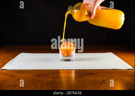 Un homme qui verse du jus d'orange dans un petit verre rempli d'oranges tranchées, Banque D'Images