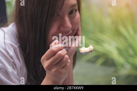Gros plan image d'une femme asiatique appréciez manger et tenir le gâteau avec la cuillère dans le café Banque D'Images