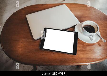Vue du dessus image maquette d'un Tablet pc noir avec écran blanc de bureau vierge avec ordinateur portable et tasse à café sur table en bois Banque D'Images
