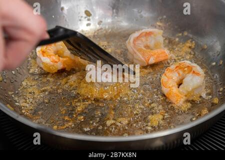 Сlose-up d'un chef mâle friture de grandes crevettes dans l'huile d'olive sur une poêle en métal. Le processus de fabrication de la crevette, des pâtes Banque D'Images