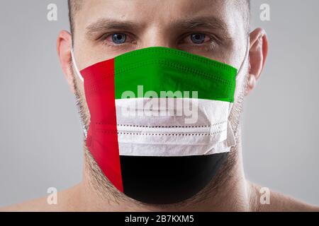 Jeune homme aux yeux douloureux dans un masque médical peint dans les couleurs du drapeau national des Émirats arabes Unis. Protection médicale contre le dis Banque D'Images