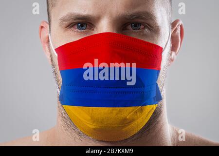 Jeune homme aux yeux douloureux dans un masque médical peint dans les couleurs du drapeau national de l'Arménie . Protection médicale contre les maladies aéroportées, coron Banque D'Images