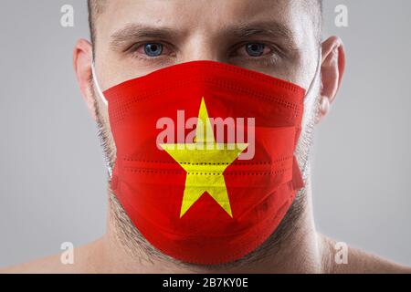 Jeune homme aux yeux douloureux dans un masque médical peint dans les couleurs du drapeau national du Vietnam . Protection médicale contre les maladies aéroportées, coron Banque D'Images