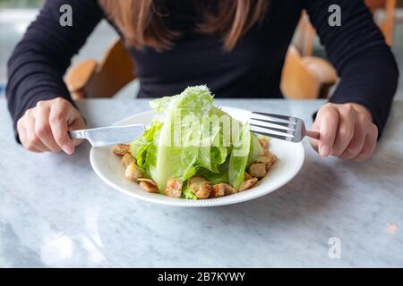 Gros plan image d'une femme mangeant une salade césar par couteau et fourchette sur table dans le restaurant Banque D'Images
