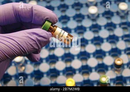 Une main portant un gant en caoutchouc nitrile contient un petit flacon étiqueté COVID-19 Coronavirus dans un laboratoire scientifique. Banque D'Images
