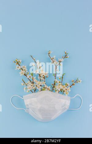 Un bouquet de branches fleuries dans un masque médical sur fond bleu avec un espace de copie, le concept de coronavirus COVID-19 au printemps 2020 Banque D'Images