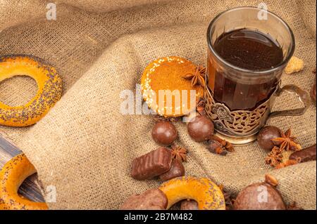 Un verre à facettes de thé dans un porte-gobelet millésime , chocolat, bagels et pain d'épices au chocolat sur fond de tissu grossier. Gros plan Banque D'Images