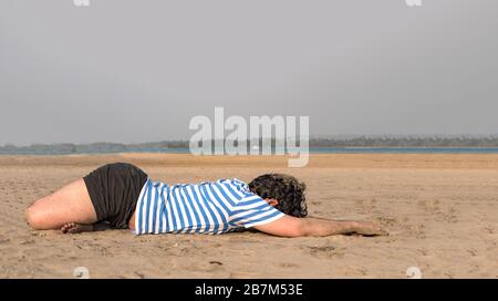 Photo latérale de jeune gars avec corps de coupe construit yoga sur la plage, en faisant la position de pli avant Lotus pour garder son corps flexible et détendu. Banque D'Images